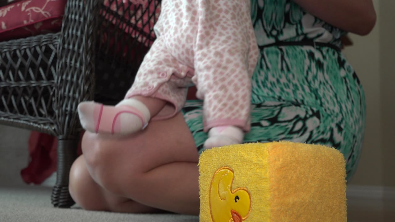 Baby's legs on a woman's lap beside a yellow duck towel.