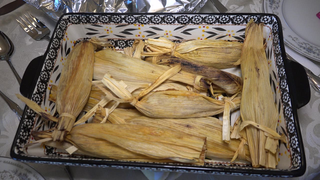 Corn-husk-wrapped food in a patterned rectangular serving dish on a table.