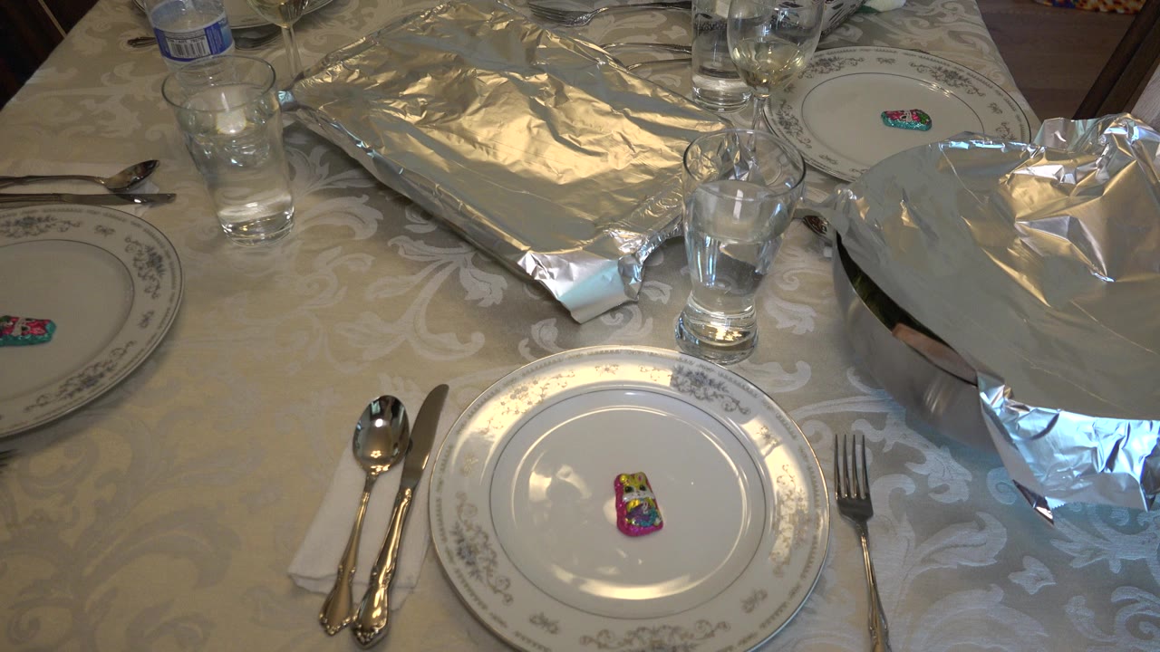 Dining table set with plates, utensils, glasses, and foil-covered dishes.
