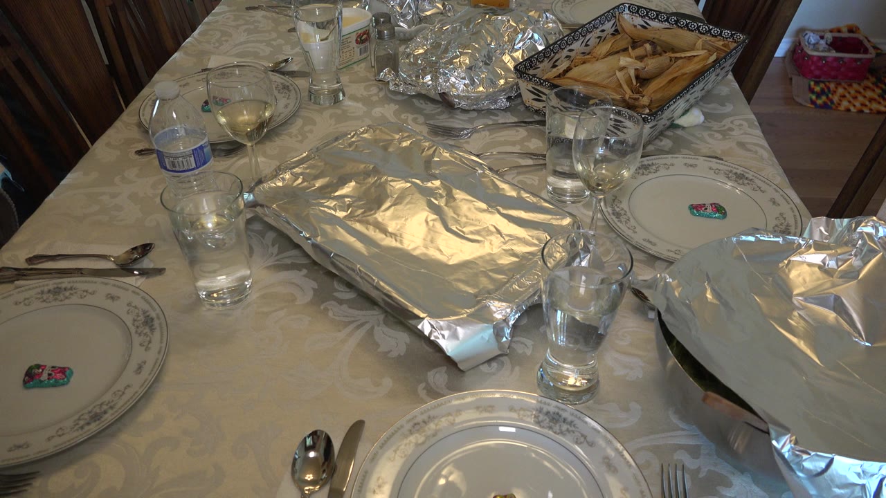White dining table with foil-covered dishes, plates, glasses, and bread basket.