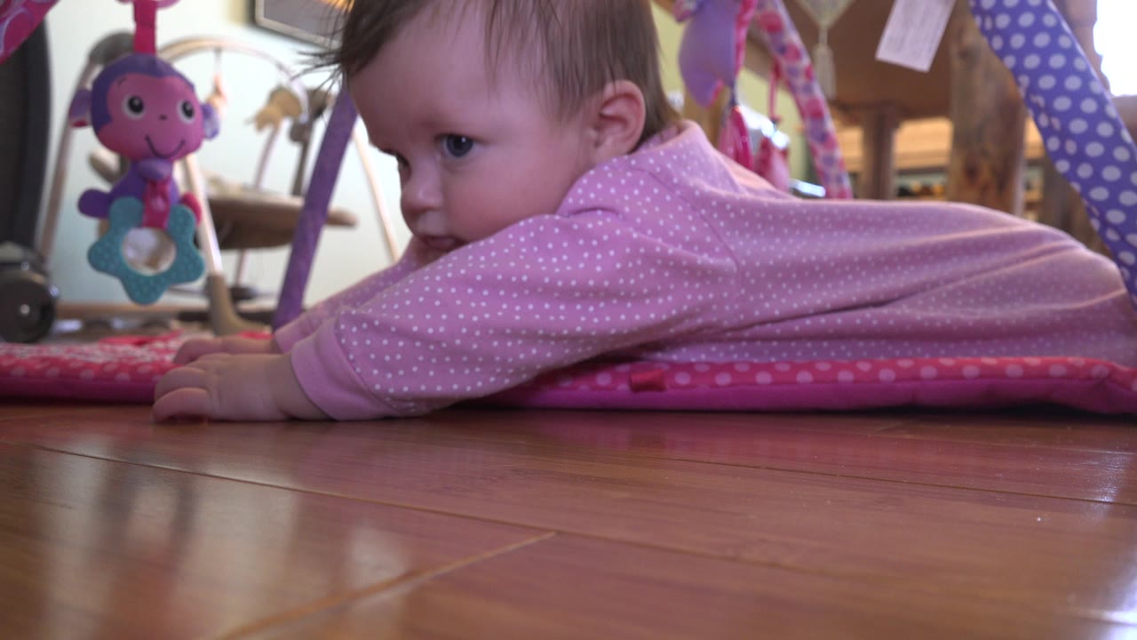 Baby turning toward the camera while lying on a pink play mat.