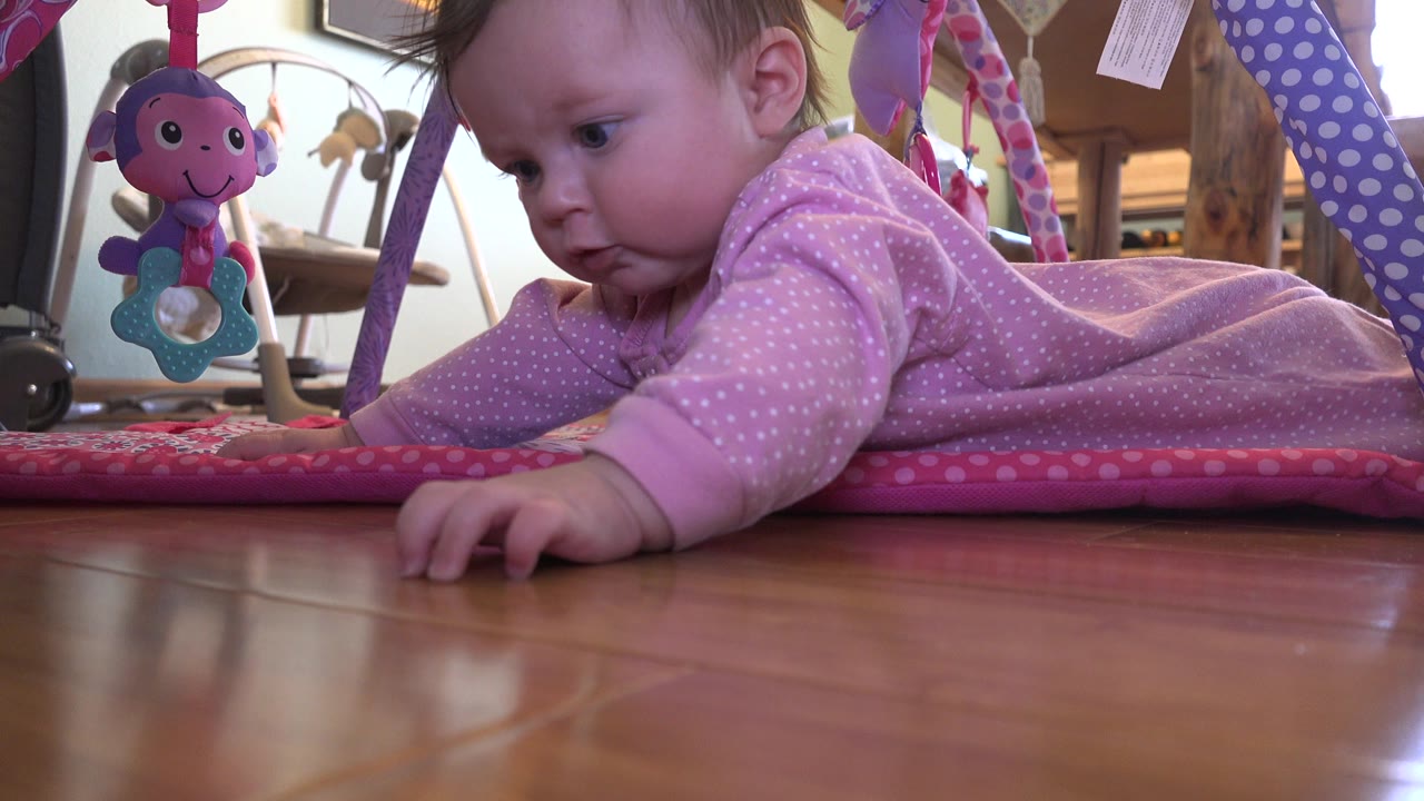 At 0:01, the baby remains close to the play mat in Westminster, Colorado, with one hand stretched forward and the hanging toy visible near the left side of the frame.