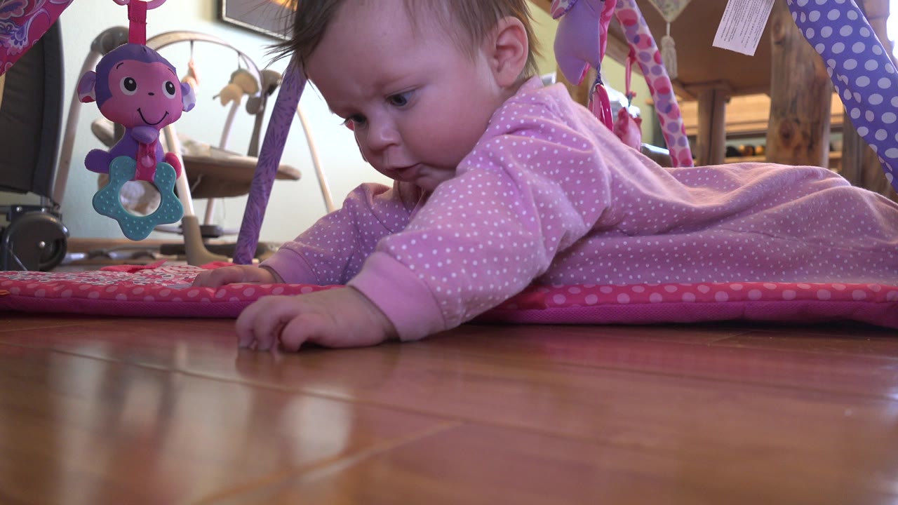 Baby leans forward on a play mat with a toy hanging nearby.