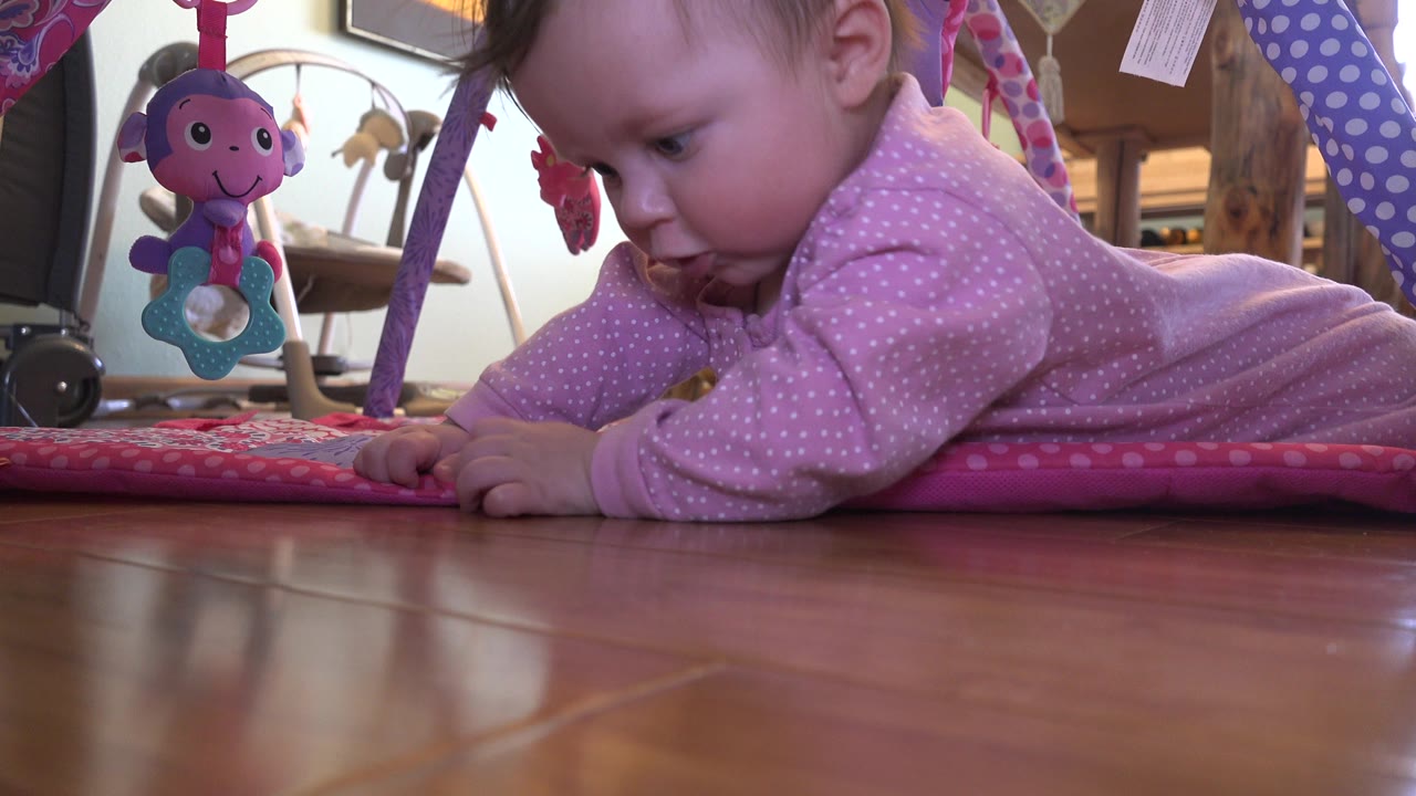 Baby lying on a pink play mat beside a hardwood floor.