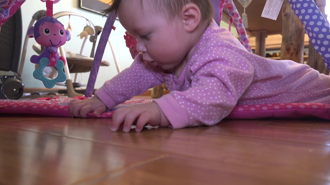 Baby crawling low on a wooden floor beside a pink play mat.