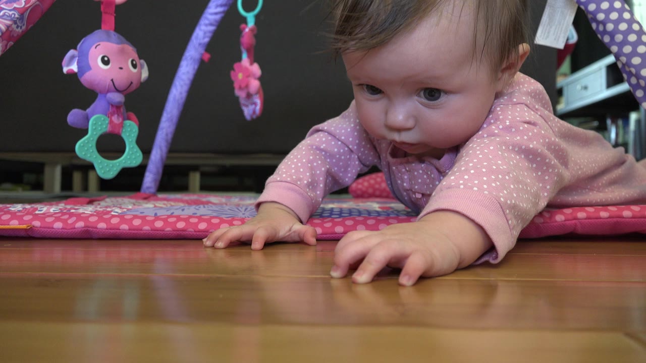 Infant in a pink onesie reaching forward on a play mat.