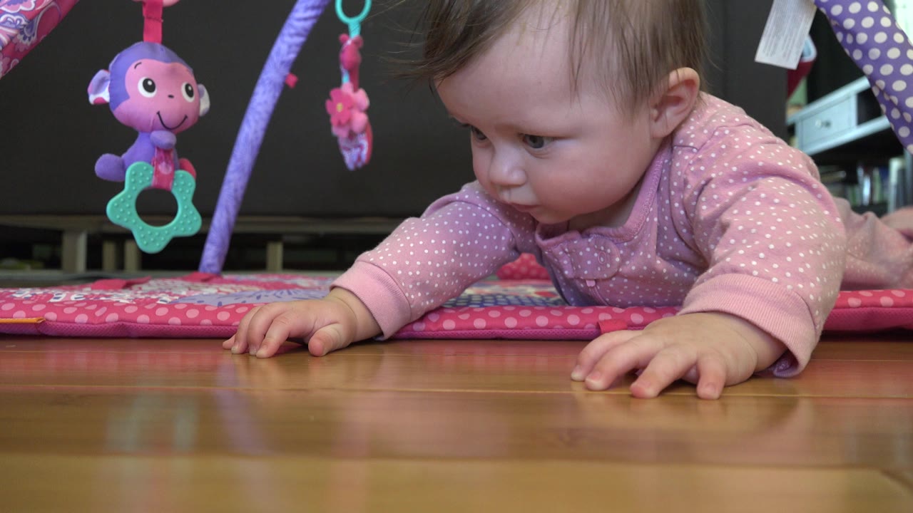 Baby lying on a pink play mat beside hanging toys.