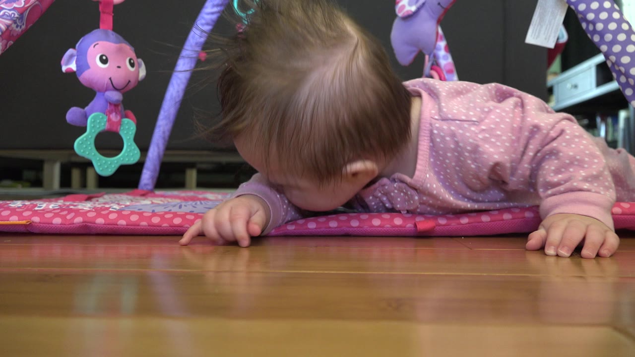 Baby in a pink sleeper lying face down on a play mat.