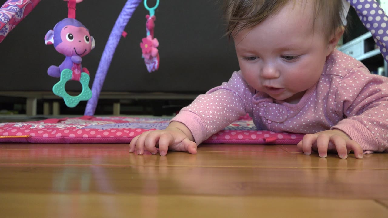 Baby lying on a pink play mat under hanging toys.