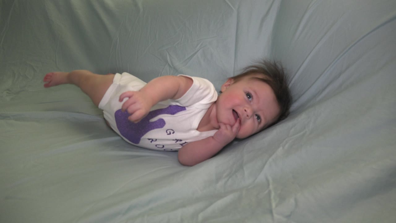 Baby girl lying on her side with hand near mouth.