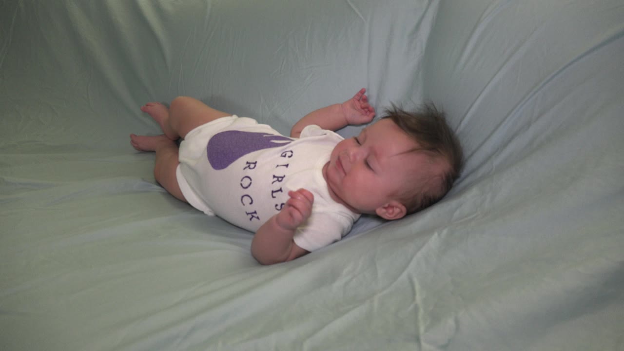 Baby lying on a pale green couch in a white onesie.