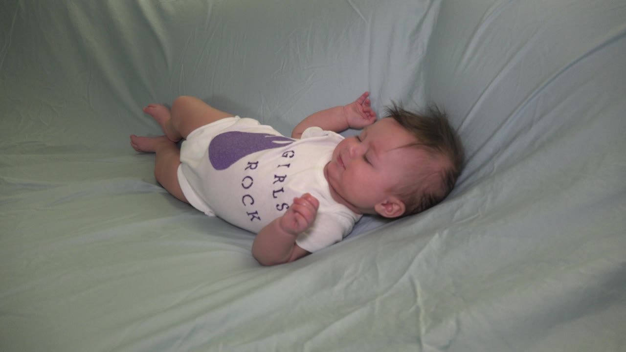 The baby remains on the pale green couch in Westminster, Colorado, with the white onesie visible and the face turned upward during a quiet resting moment.