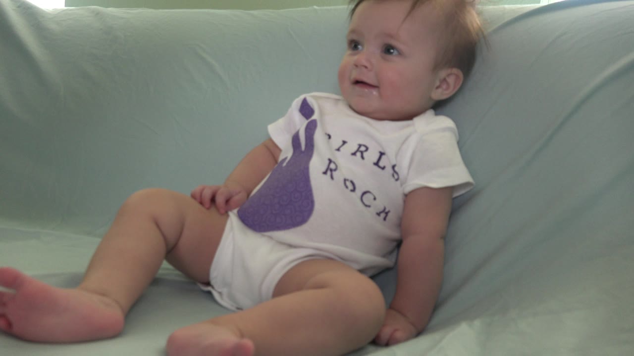 Baby reclines on a pale green couch in a white onesie.