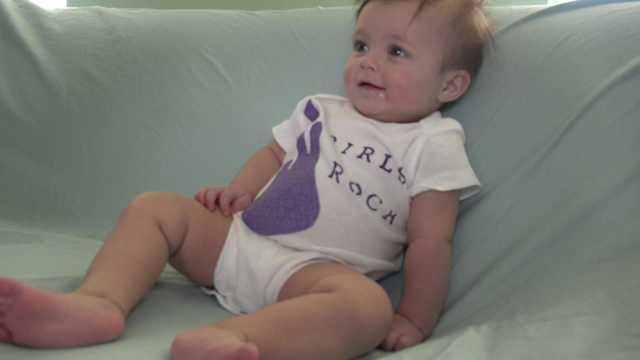 In Westminster, Colorado, the baby remains reclined on the pale green couch, looking up and slightly to the side while one bare foot extends toward the foreground.