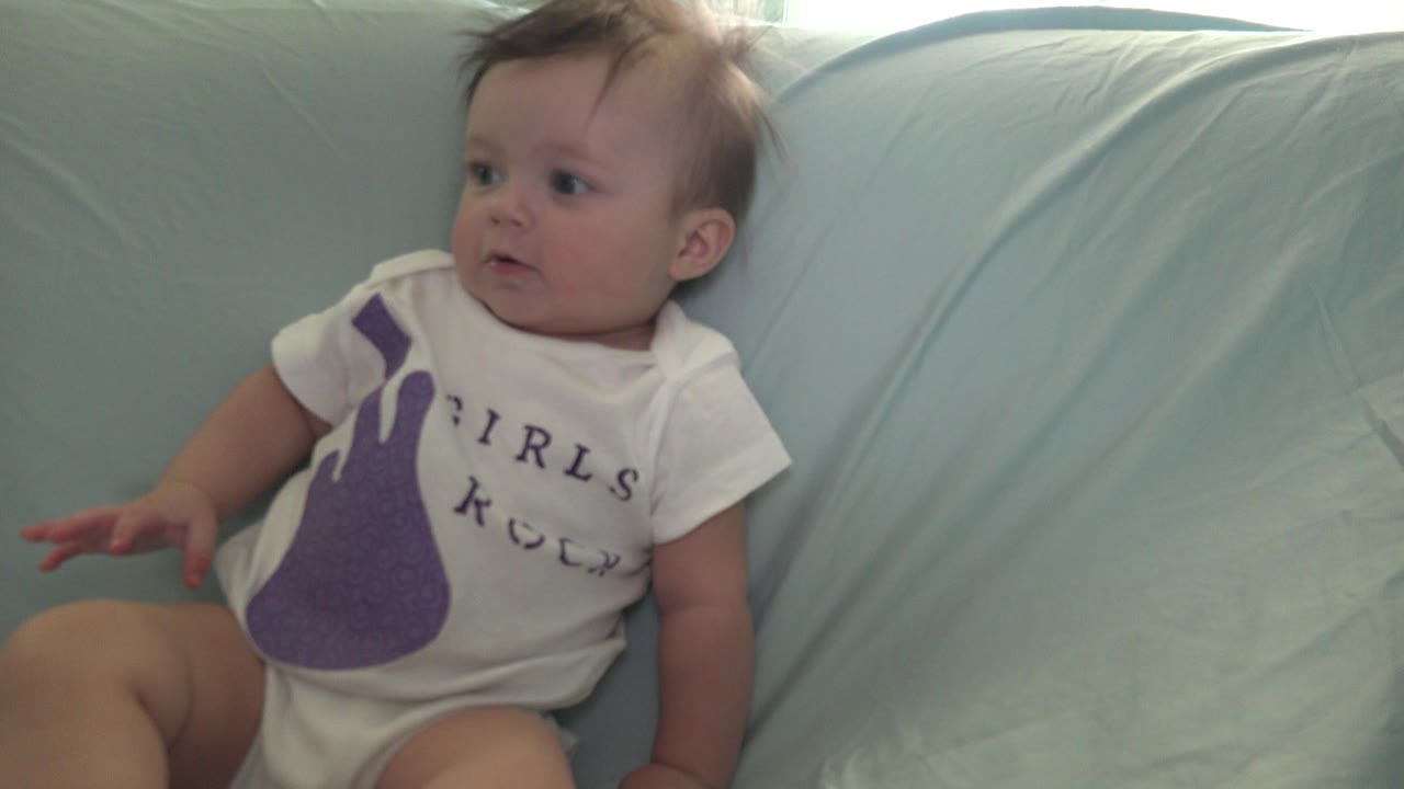 Baby in a white shirt sitting on a light green sofa.