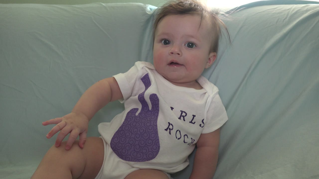 Baby sitting upright with wide eyes on a pale blue couch.