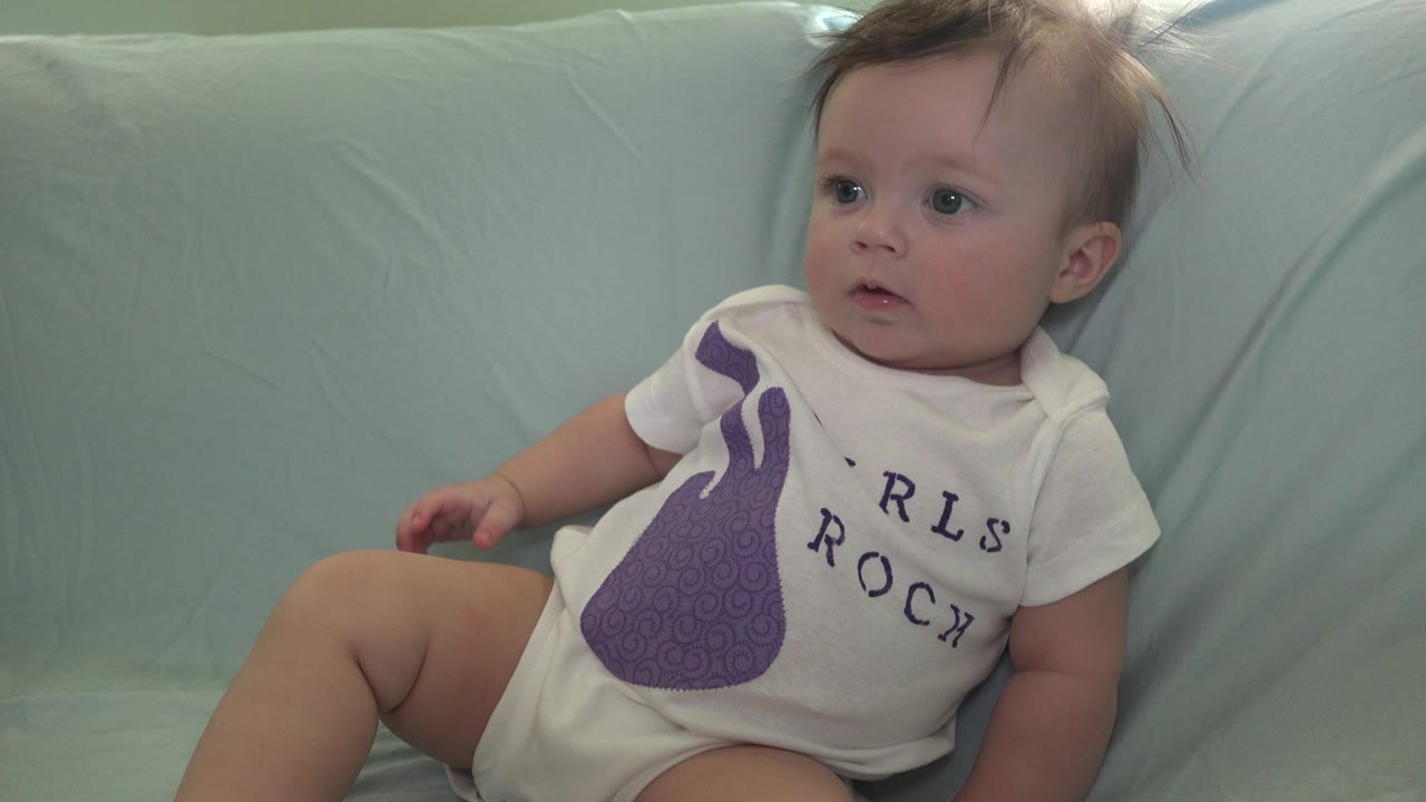 Baby seated on a pale aqua sofa looking off frame.