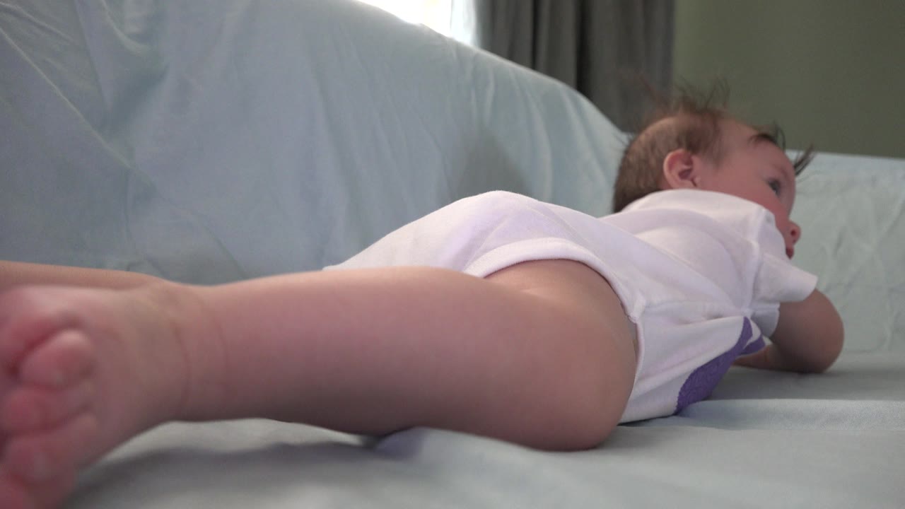Baby lying on a pale couch with bare feet close to the camera.