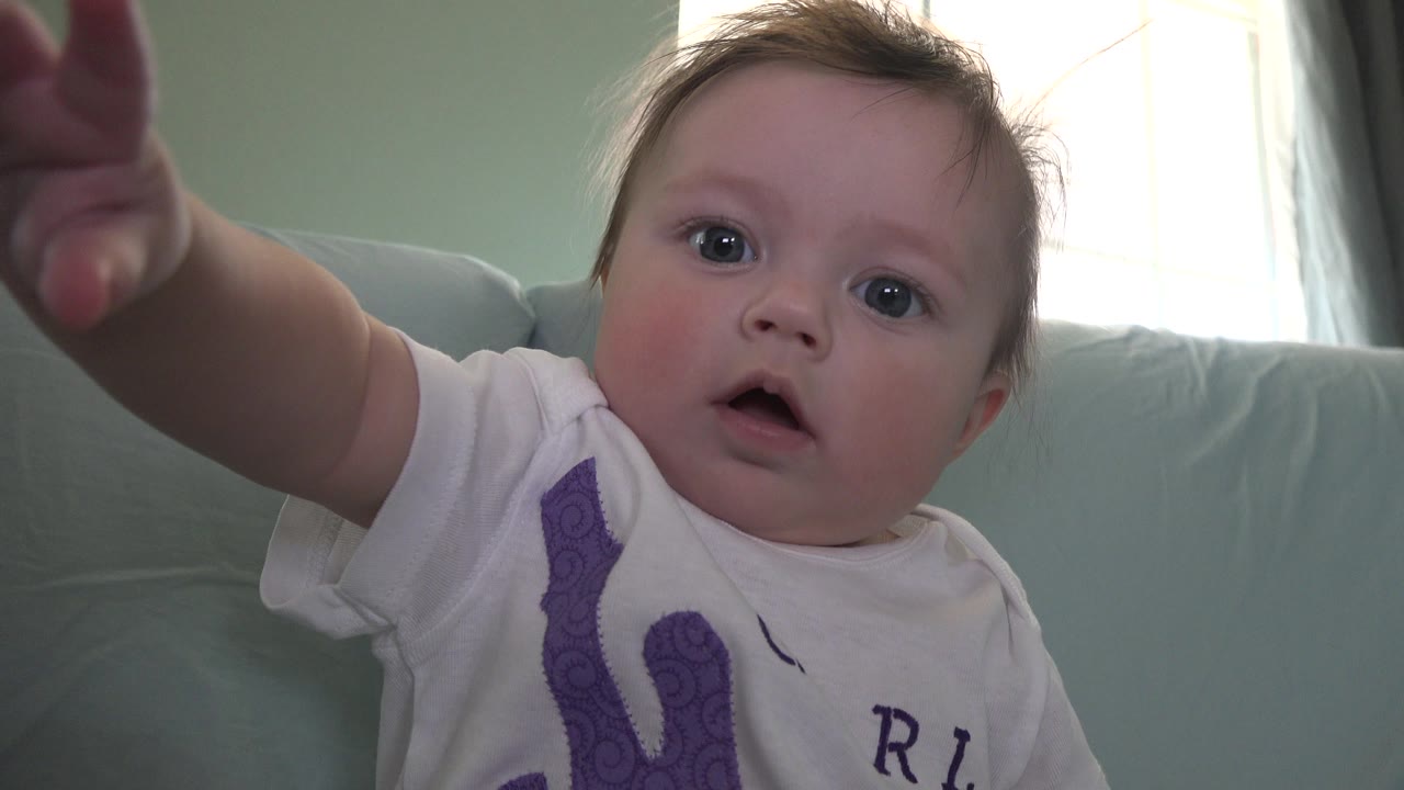 Baby with mouth open reaching upward near the camera.