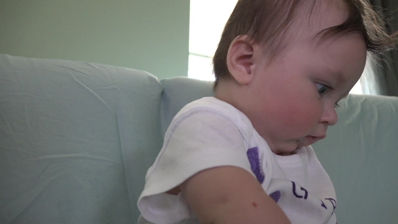 Baby in a white shirt sitting sideways on a light green sofa.