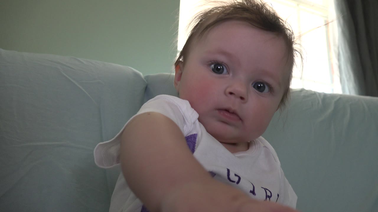 A Westminster, Colorado baby faces the camera from a low angle, with one arm reaching forward and the pale blue sofa behind her.