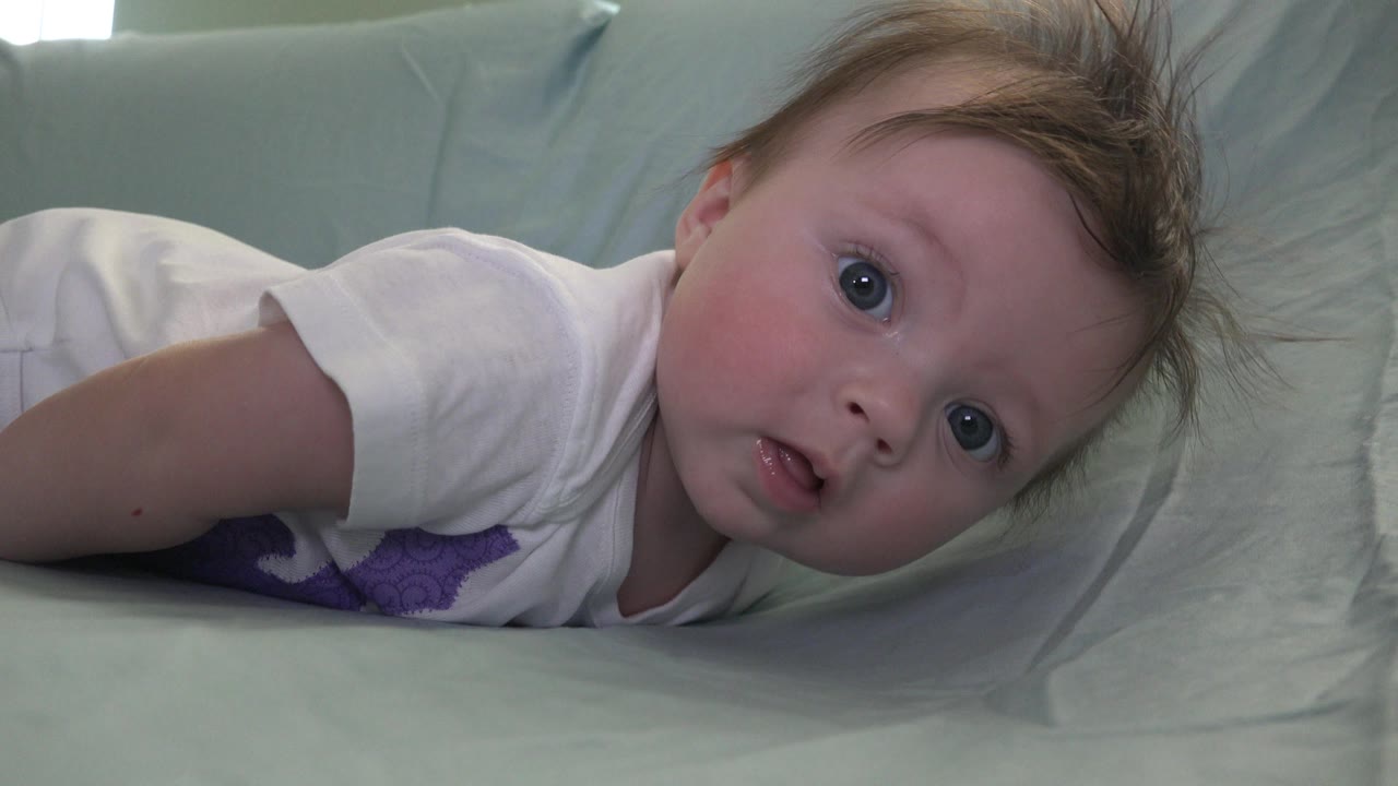 Baby lying sideways on pale bedding and looking toward the camera.