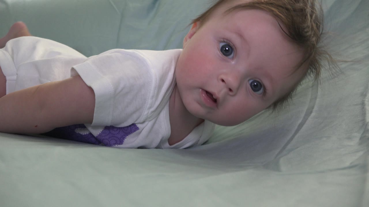 The baby appears a little more upright on the pale bedding in Westminster, Colorado, with wide eyes, tousled hair, and the pillow filling the background.