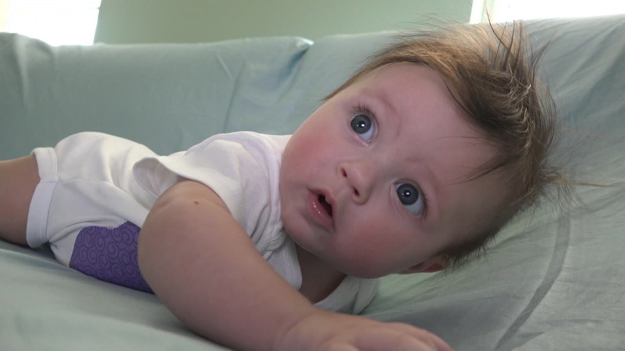 Baby boy lying on a pale green cushion and looking upward.