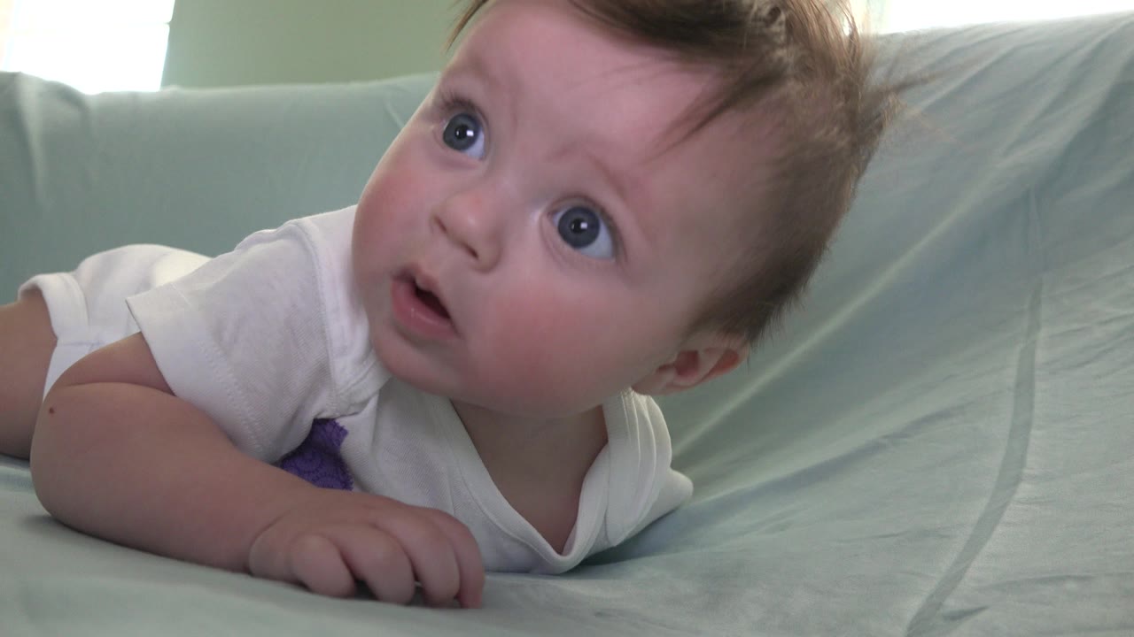 Blue-eyed baby lying on a pale blue couch and looking upward.
