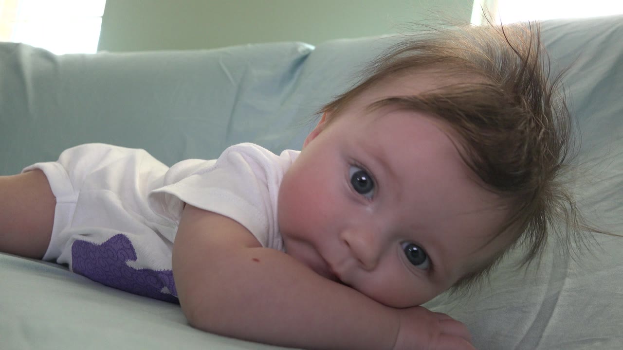 Baby lying on a pale bed with blue eyes looking toward camera.
