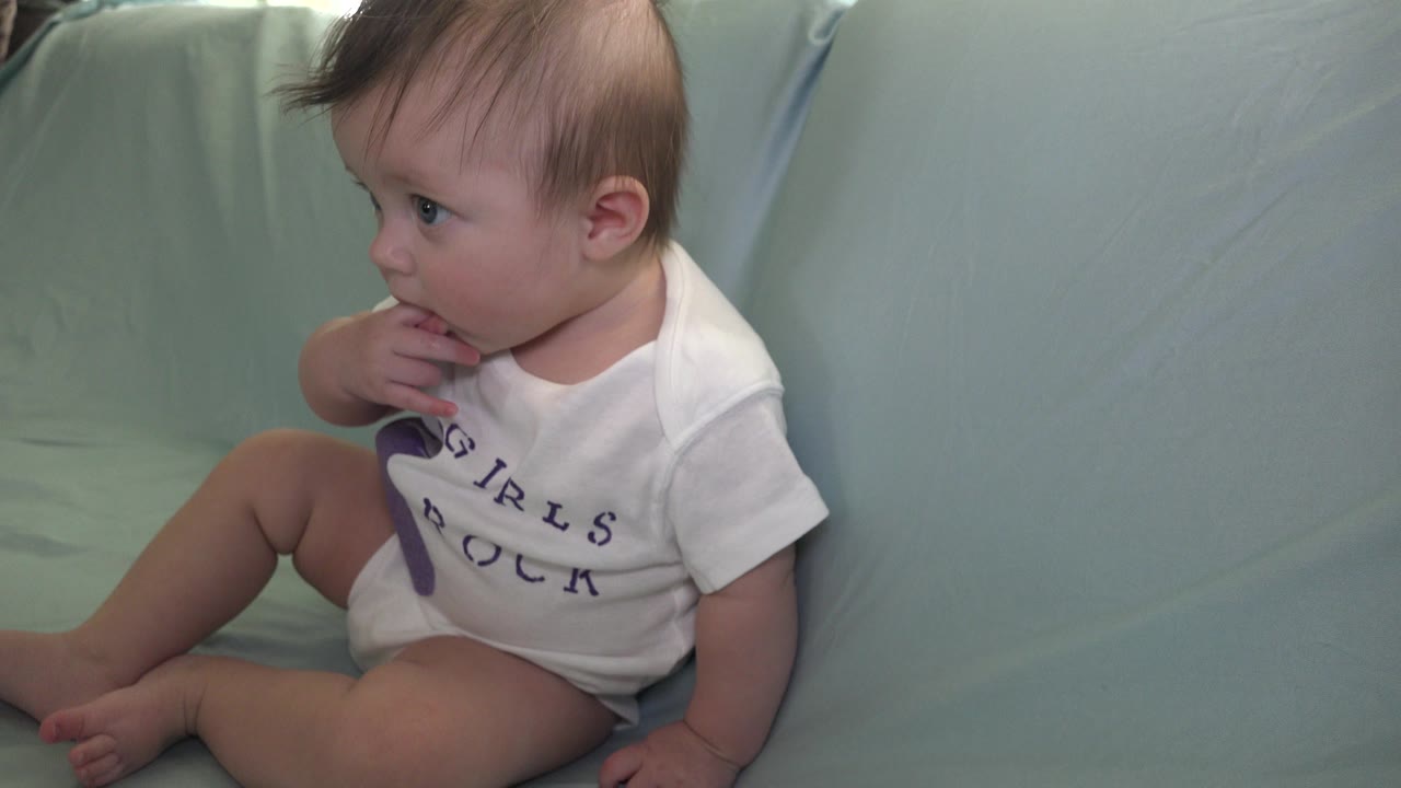 Child on cushion with knees bent and fingers at lips.