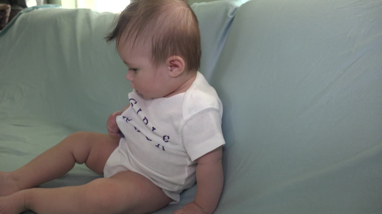 Infant on a blue sofa turning slightly to the side.