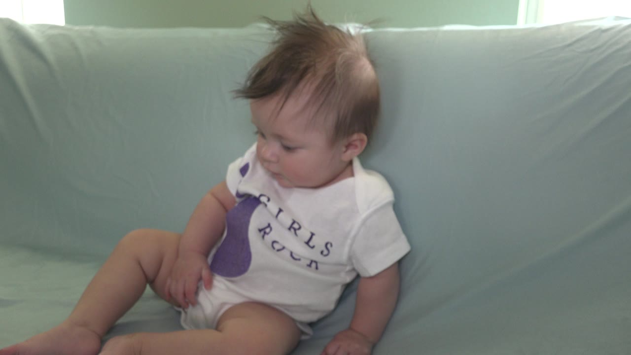 The baby sits farther to the right in frame on the pale blue couch in Westminster, Colorado, with tousled hair and the face angled toward the lap.