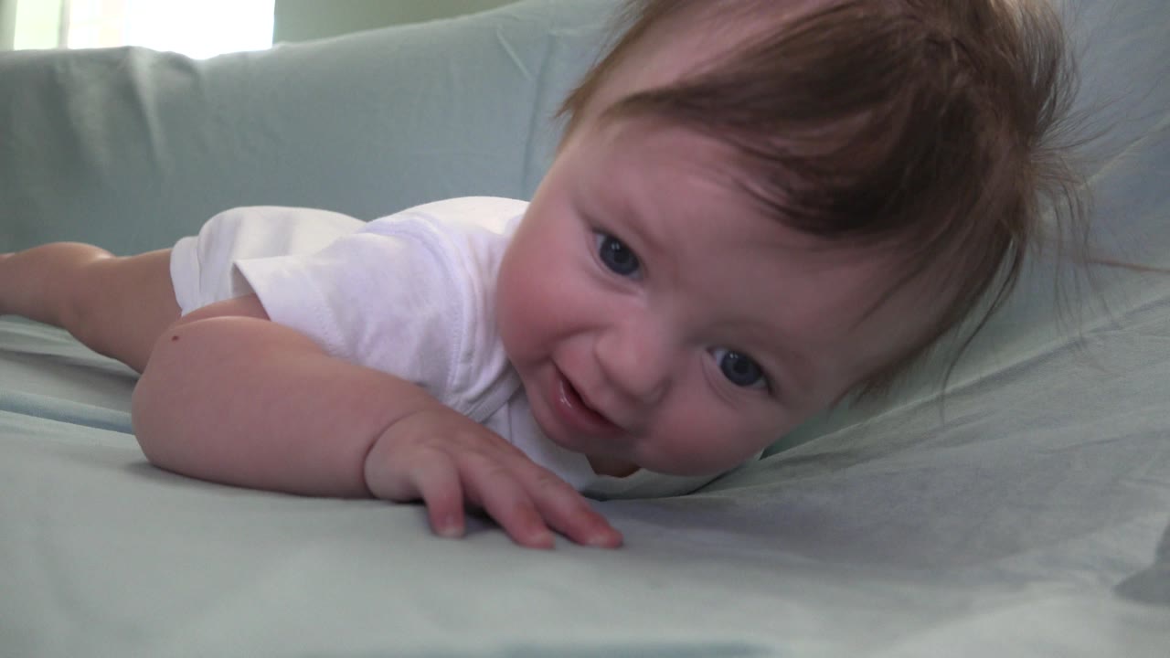 Baby lying on a pale covered sofa in a white shirt.