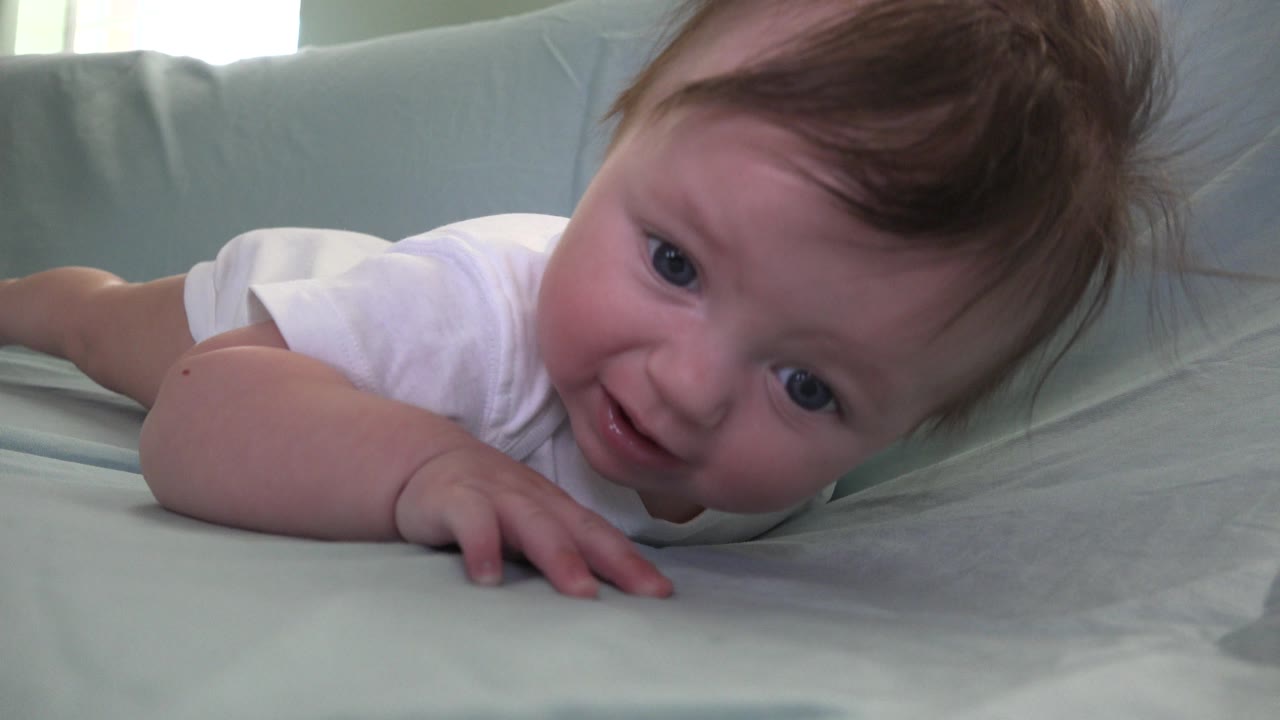 At 0:01, the baby remains on the pale sofa cover in Westminster, Colorado, with the face closer to center and a hand pressed into the fabric.