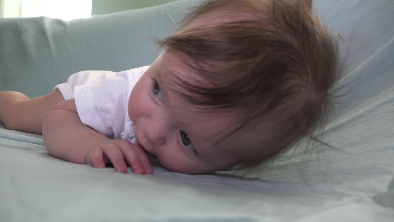 Infant lying on a pale sofa with one hand on the sheet.