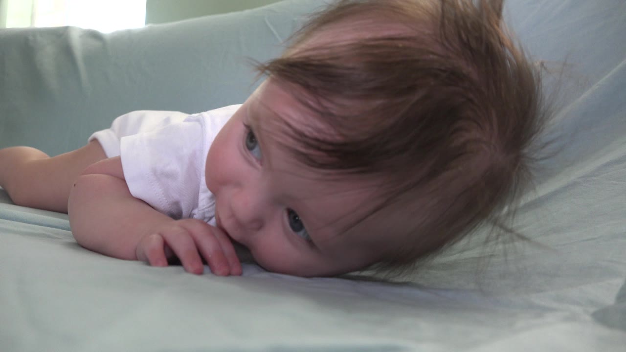The infant remains on the sofa in Westminster, Colorado, with the face turned slightly forward and small fingers pressed into the pale fabric.