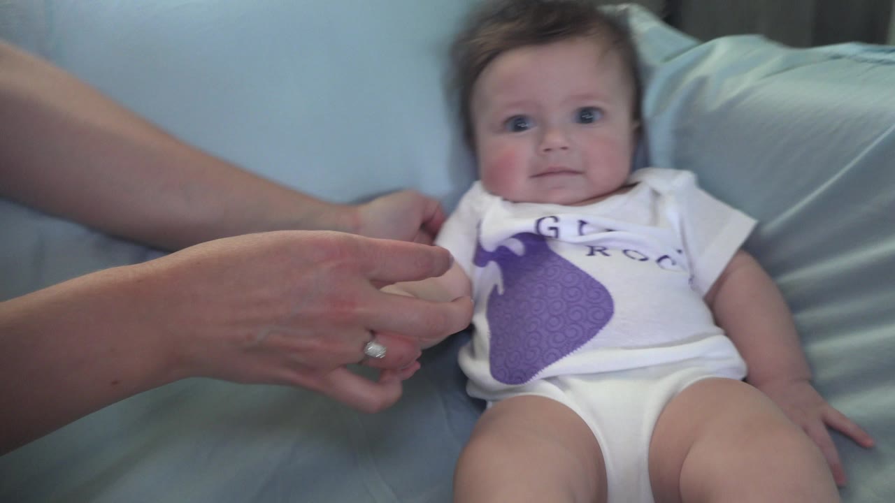 Adult hands adjust a baby lying on a couch.