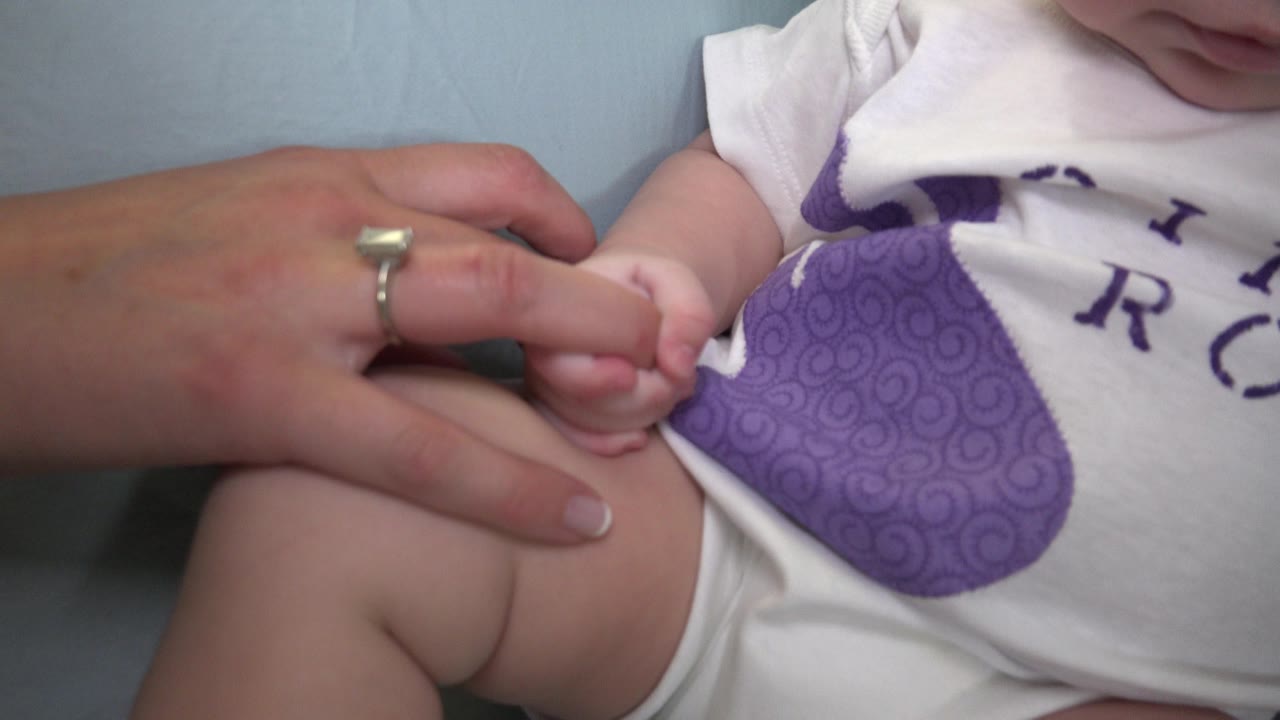 Baby's hand touching an adult finger near a purple-printed onesie.