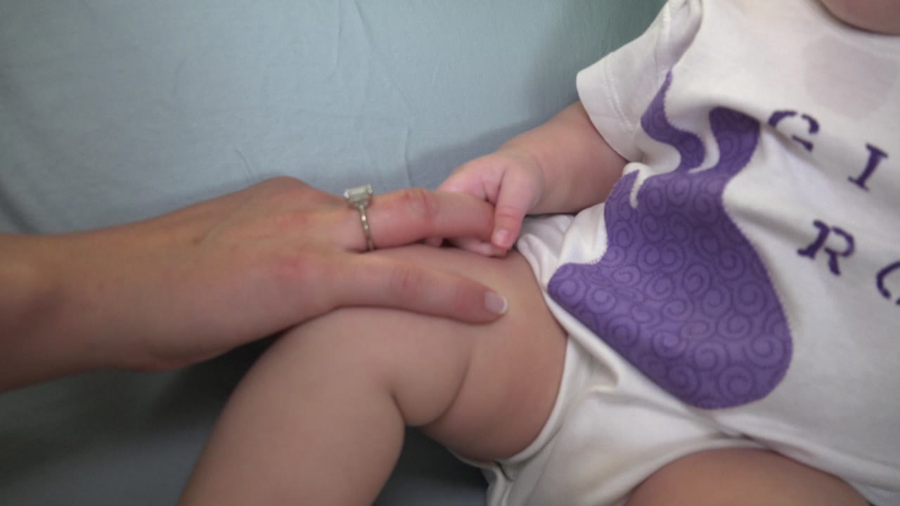 Adult hand holding a baby's small hand near the baby's lap.
