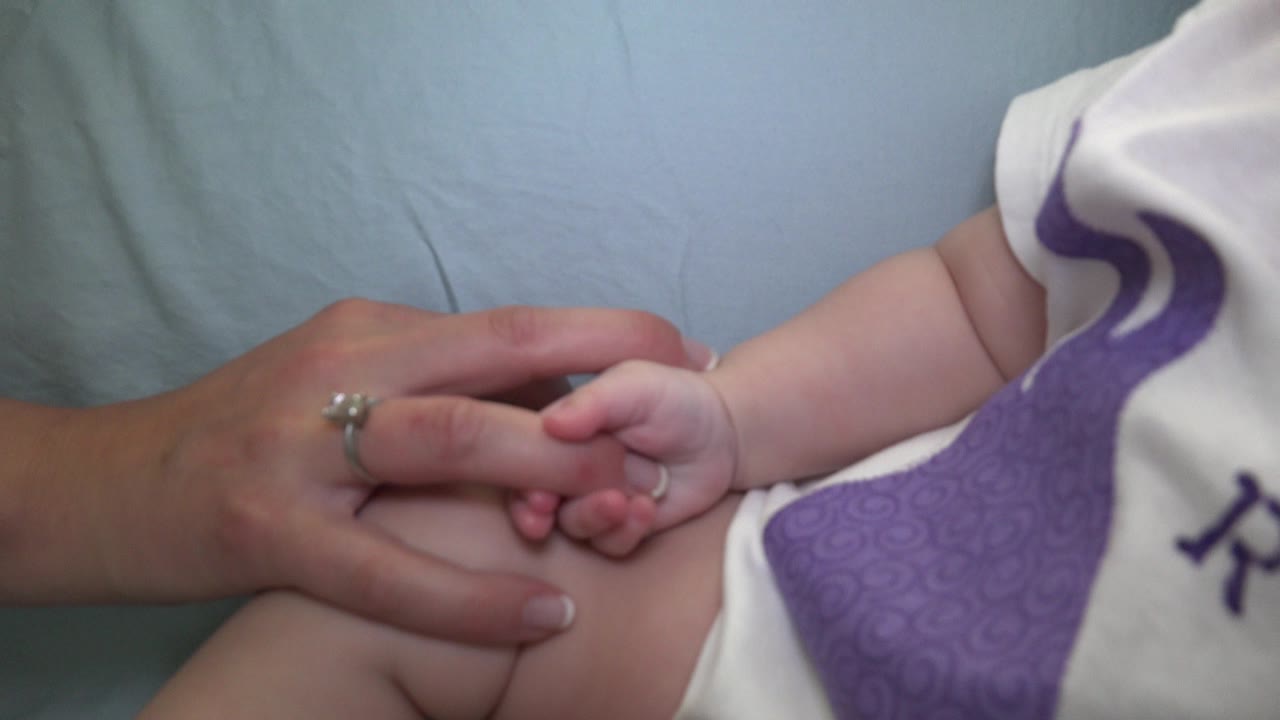 At 0:01 in Westminster, Colorado, the mother's hand rests across the baby's leg while the infant's fingers hold near the adult index finger.