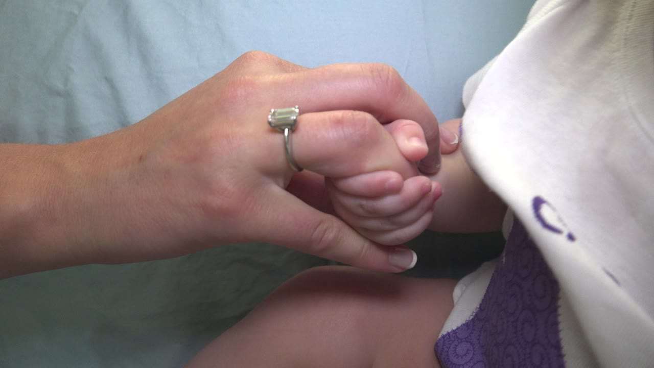 The second frame keeps the adult hand centered around the baby's curled fingers, with the baby's arm and white clothing partly visible at the right edge.
