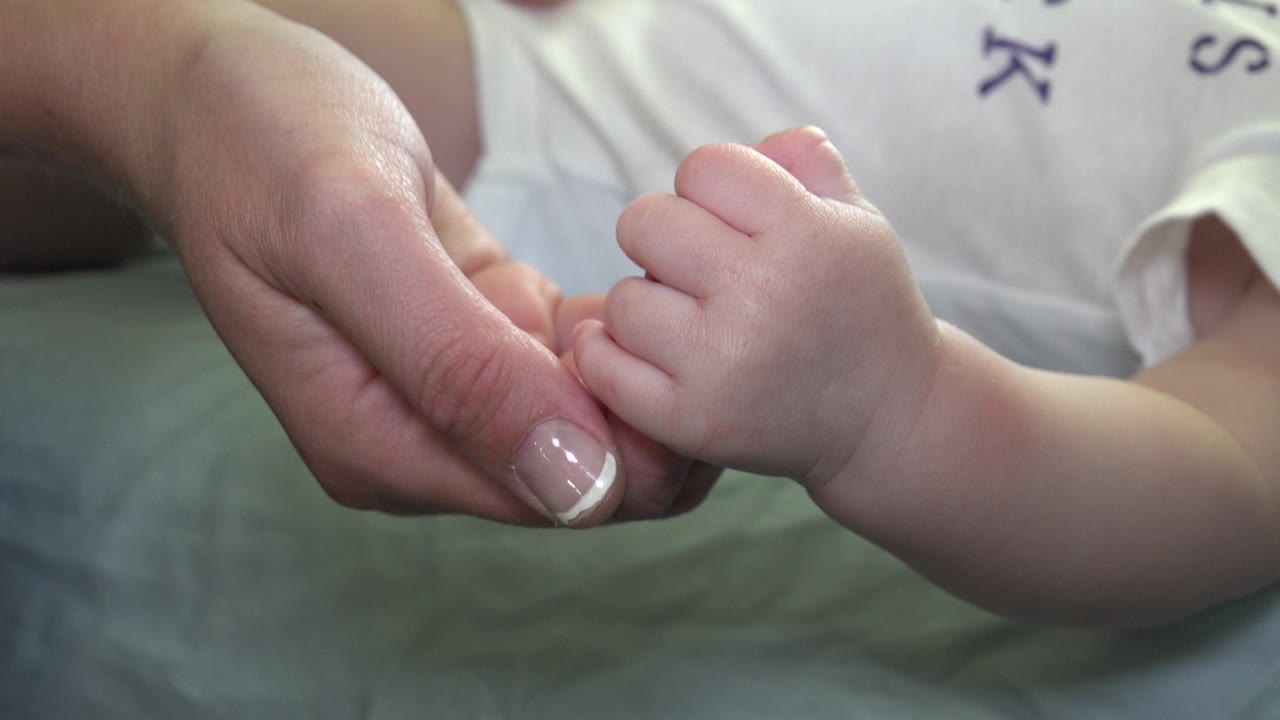 Baby foot held near an adult hand in soft indoor light.