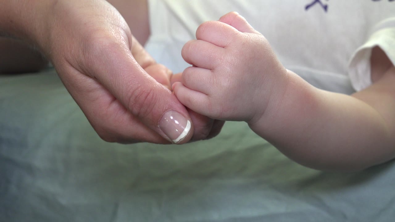 Infant hand holding an adult finger over green bedding.