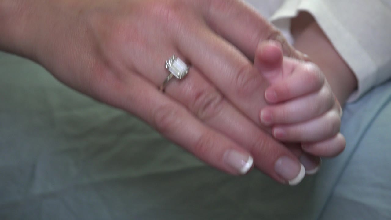 Adult hand with diamond ring holding an infant hand.