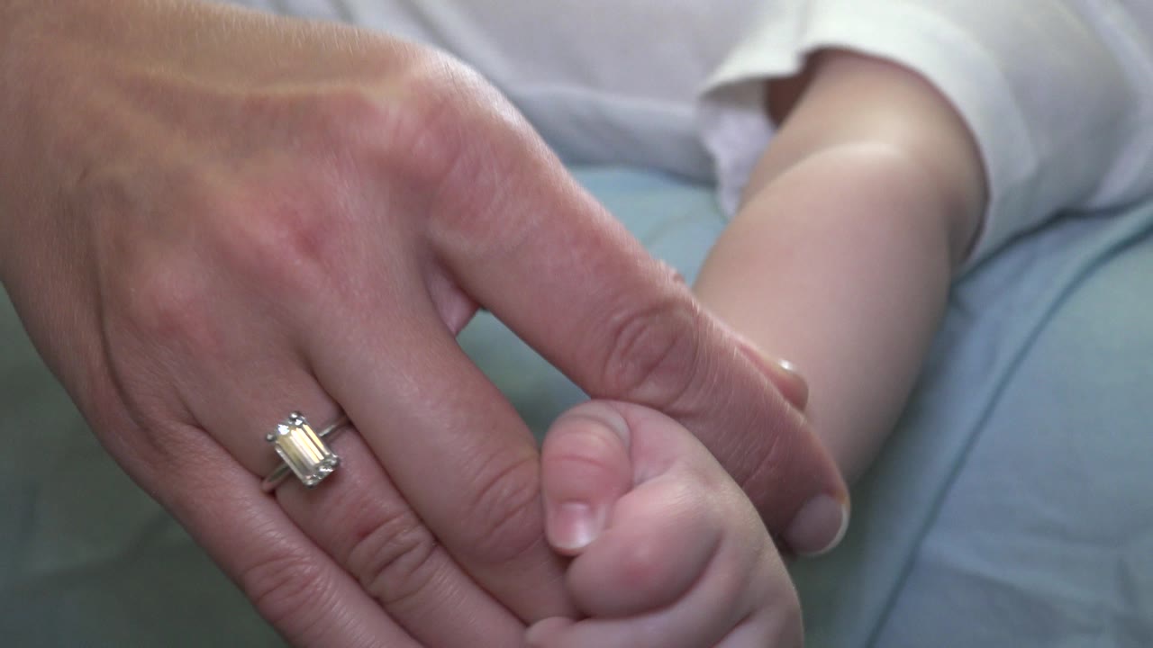 Adult hand holding a small child's hand on a bed.