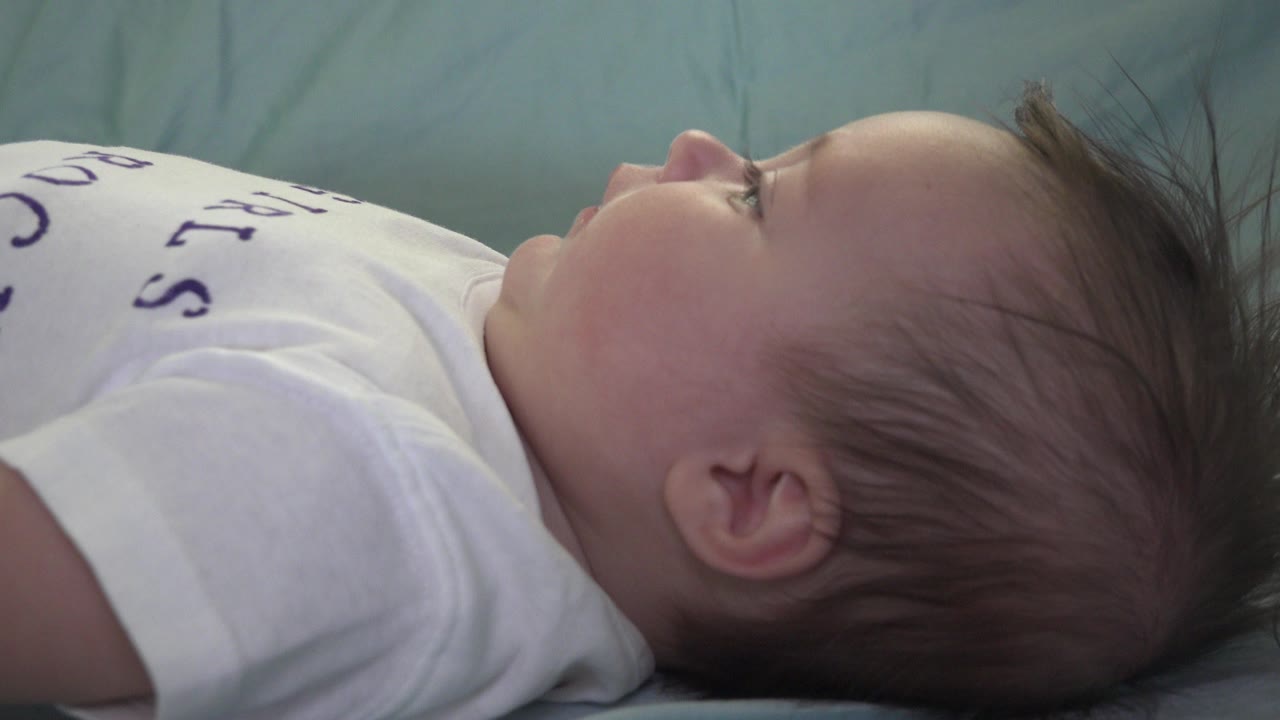 Baby lying sideways on a blue-green bed in a white T-shirt.