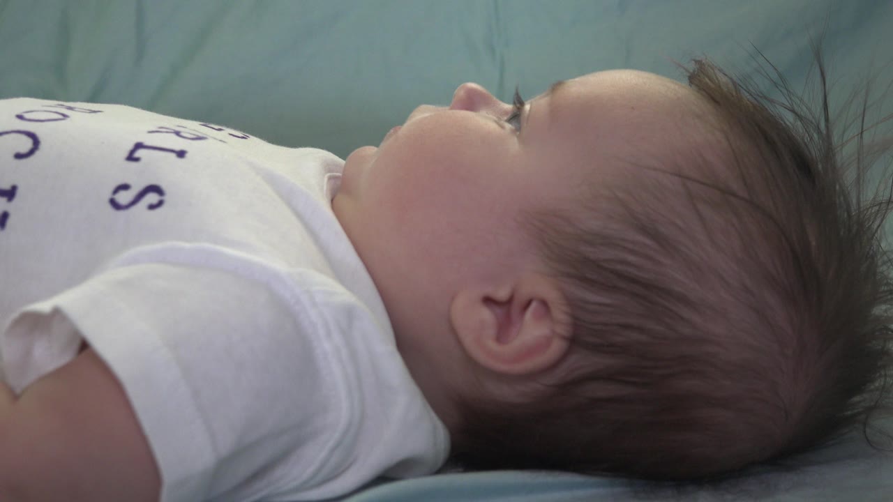 Baby lying sideways on pale blue bedding in a white shirt.