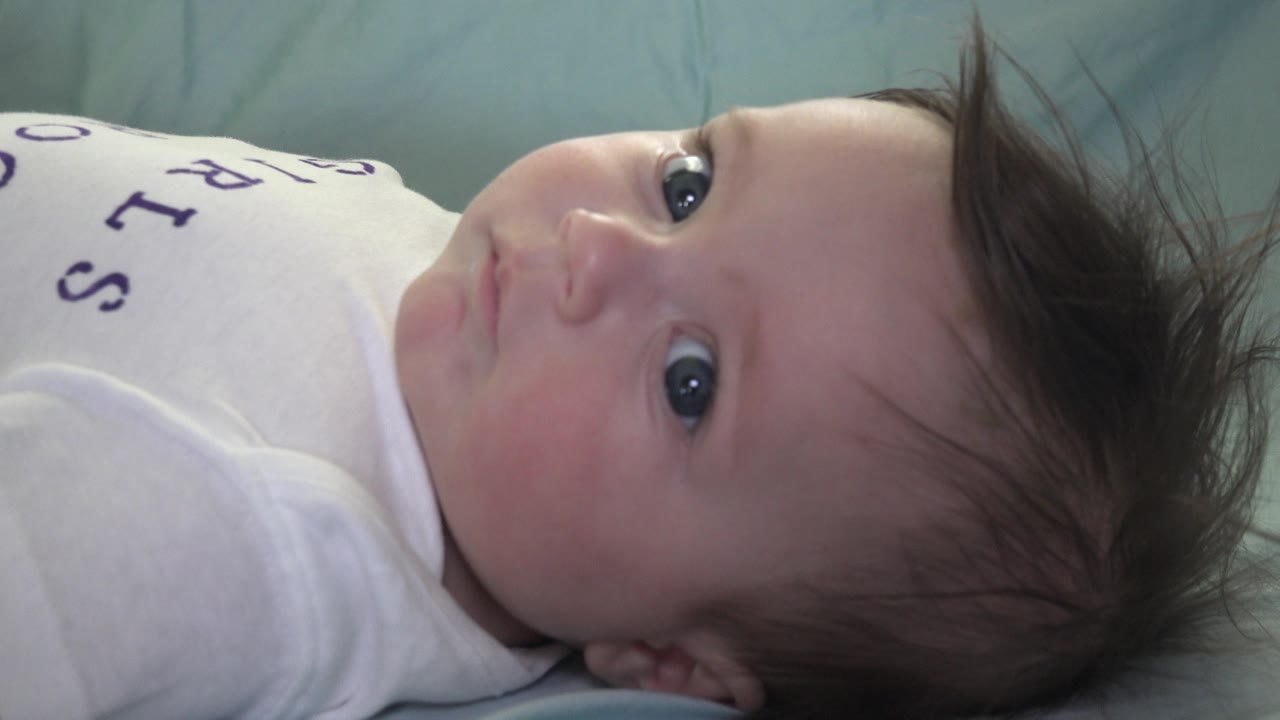 Baby in a white shirt looking sideways on a green blanket.