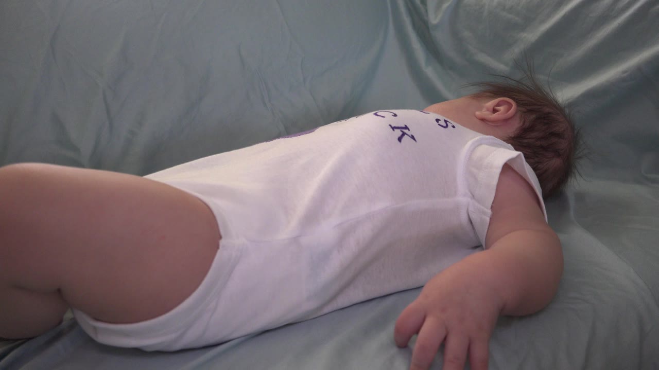 Baby lying on a pale sheet in a white romper.